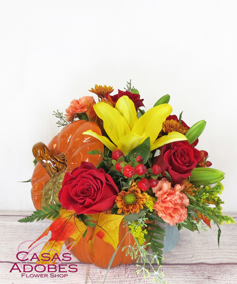 Pumpkin shaped container with yellow lily, orange carnations red roses, berries, fall oak leaves