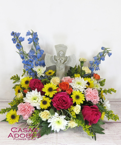 Keepsake cross with an angel in the center. The cross is a faux stone look. Spring flowers include blue delphinium, pink carnations, yellow daisy and solidaster.