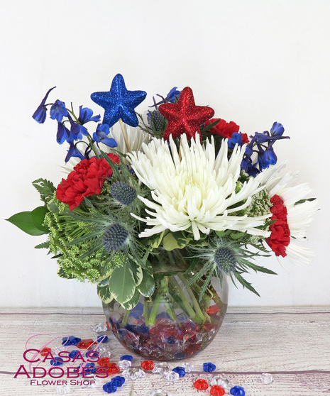 white mums, red carnations, blue delphinium in a bubble bowl vase with star shaped gems